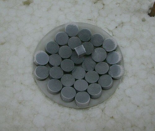 時計の皿の上の濃い灰色の錠剤。錠剤の上に同じ材質の立方体のピースが 1 つあります。