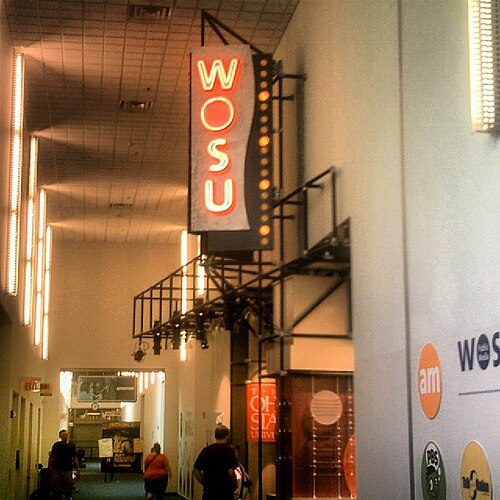屋内廊下の展示スペースに「WOSU」と書かれた大きな縦看板
