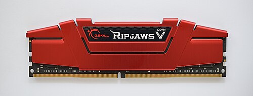 オレンジ色の金属製ヒートシンクがRAM ICを覆っており、RAM ICはヒートシンクの下にあるプリント基板にはんだ付けされています。ヒートシンクの下には、プリント基板の一部が緑色の帯として見えます。コンピューターに挿入される金色の接点は、一番下にあります。