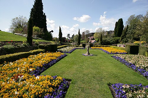 晴れた空の下、手入れされた芝生、花壇、石の台座を備えたフォーマルな庭園