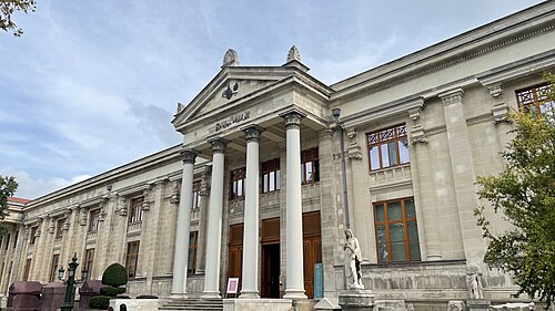 澄み切った青空の下、入り口を飾る4つのギリシャ像のある石造りの建物のファサード