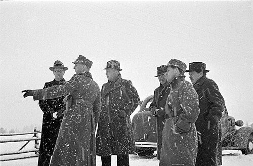 フィンランドとソ連の国境紛争が冬戦争にエスカレートしたマイニラで、外国人ジャーナリストの一団が雪が降る中、何かを観察している。