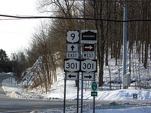 2 つの高速道路の交差点の前にある一連の道路標識。交差点の後ろの丘は雪に覆われ、頭上には電線が垂れ下がっています。