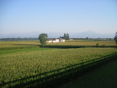 前景に農家と農作物、遠くに山々が見える田園風景の写真。