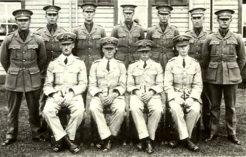軍服を着て山高帽をかぶった男性11人の肖像画。7人が立っており、4人が座っている。