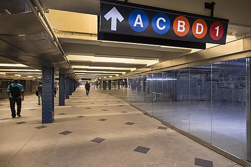59 番街 - コロンバス サークル駅の中二階。右側に店舗があります。矢印、「A」、「C」、「B」、「D」、「1」のアイコンが描かれた看板が天井から吊り下げられています。