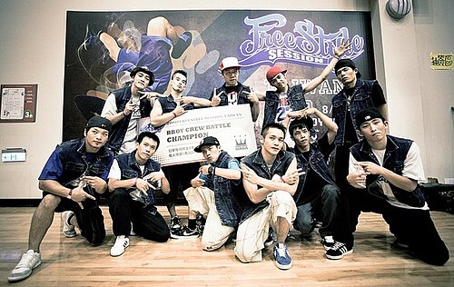 「フリースタイルセッション台湾」と書かれた横断幕の前で、「BBoy Crew Battle Champion」と書かれた大きな看板を掲げながらポーズをとる 11 人の若者のグループ。
