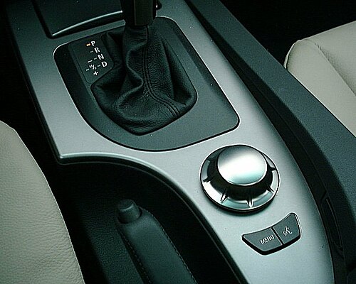 上部に黒いシフトレバーが付いた、銀色の車のセンターコンソール。その下には円形の銀色のノブがある。