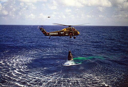 緑色のヘリコプターが水面上を低空飛行しており、その下にはマーキュリーカプセルが吊り下げられている。ヘリコプターには「海兵隊」と書かれており、「44」という数字が刻まれている。