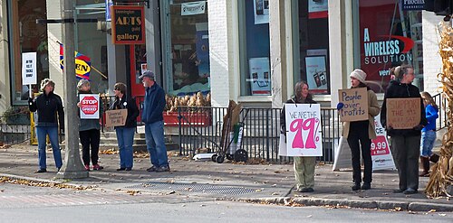 街路沿いに、手書きの段ボール製プラカードを持った7人のグループ。一番大きなプラカードには「私たちは99％だ」と書かれている。