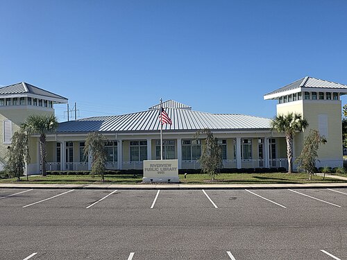 リバービュー公共図書館の昼間の写真。中央のポールにはアメリカ国旗が掲げられている。建物は薄い黄色で、縁取りも黄色。