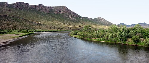 茂みと開けた地面の間を流れる暗い川は、高い尾根を避けるために曲がっています。