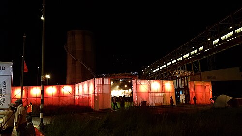 大きなオレンジ色に輝く赤いフェンスの周りをうろつく人々のシルエットを夜間撮影したもの