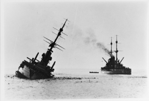 戦艦は魚雷に撃たれて大きく傾き、水面下で沈んでいます。近くには別の戦艦が浮かんでいるのが見えます。