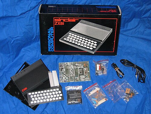 ZX81 のケース、キーボード、回路などの構成部品は、出荷時に使用された段ボール箱の前にある青いシートの上に置かれています。