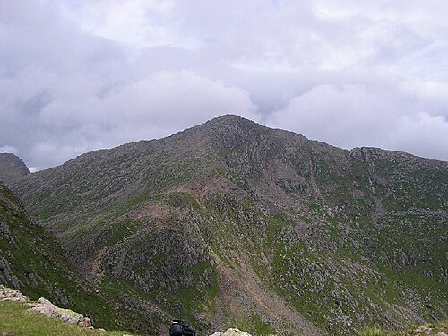 紫色のヒースと緑の植物で覆われた山の側面。背景には青灰色のふわふわした雲が広がっています。