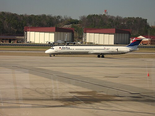 デルタ航空の MD-88 が、バーミンガム・シャトルズワース国際空港で、アメリカ空軍州兵第 117 空中給油航空団の 2 つの格納庫、第 117 KC-135 戦闘機、空港消防署を通り過ぎて走行しています。