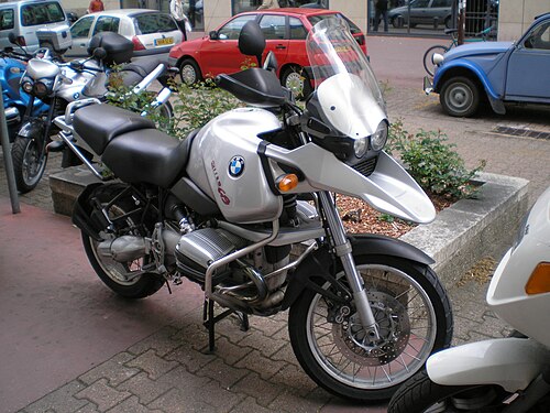 銀色の BMW R1150GS が市街地に駐車され、背景には他の車やバイクが並んでいる