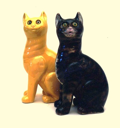 黒い陶器の猫が黄色い陶器の猫の隣に座っています。