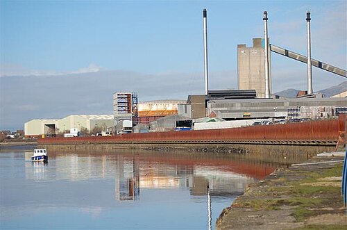 水辺の岸辺にある大きな塔のあるガラス工場の建物
