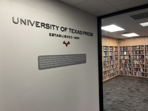 UT Pressのオフィスの写真。壁にはロゴと社名が掲げられ、背景には本棚が写っている。