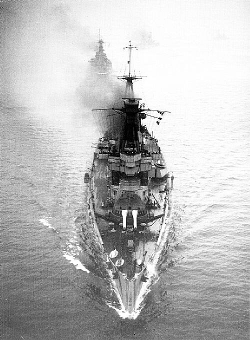 大型軍艦を見下ろした写真。この軍艦は高速で航行しており、撮影者の下を 2、3 隻の他の大型船が通過しようとしています。
