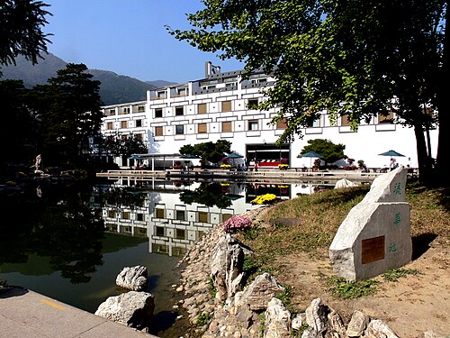 装飾された窓のある白い建物、フレグラント ヒル ホテルは、岩の構造物に囲まれた湖に面しています。建物の周囲には木々が生い茂っています。