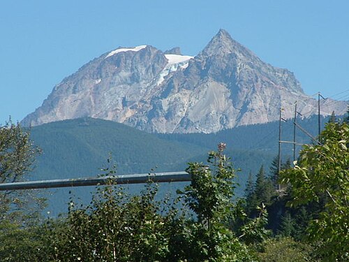 頂上にはほとんど雪がなく、前景の丘陵の植物に覆われた地形を見下ろす岩山。