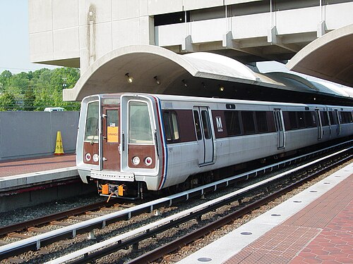 駅のホームに停車中の、特徴的な茶色とメタリックなデザインの列車を、外観から遠近法で捉えた写真。