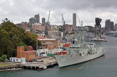 灰色に塗装された軍艦 2 隻が埠頭に停泊しているカラー写真。船の後ろには大きなクレーンといくつかの建物が見える。