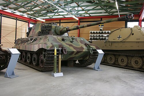博物館に展示されている、平らな砲塔を備えた大型戦車の3/4正面図。鈍い黄色、緑、茶色の波状迷彩が施されている。前面装甲は傾斜している。長砲身は車体前部から数メートル突き出ている。その前方には、腰の高さほどの弾薬が2発、台座の上に置かれている。