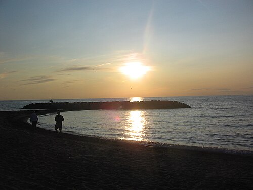 暗くなった砂浜と防波堤に夕日が沈む。
