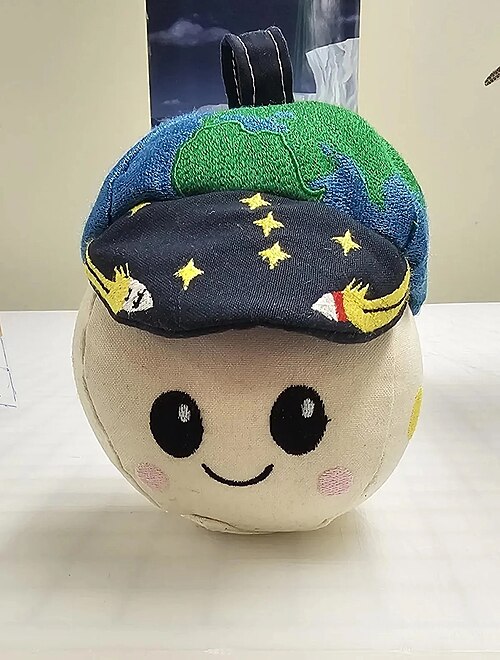アルテミスII無重力計「ライズ」。地球の帽子をかぶった、笑顔の白いボール型のおもちゃです。