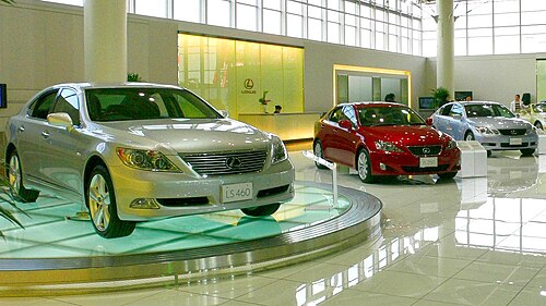 受付カウンターと窓の前に、ガラスのターンテーブルの上に最も近い 3 台のセダンを展示した自動車ショールーム。