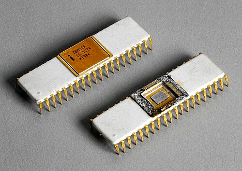 小さな白い長方形のマイクロプロセッサチップ2個をクローズアップした画像。チップの側面から下に向かって、小さな金色の金属製の突起が伸びている。左上のチップは、上部中央部分に「C8080B、ES 1274、KI984」と刻印された金色のカバーが付いている。右下のチップはカバーが取り外されており、半導体材料のダイが露出している。