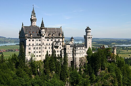 森の風景を見下ろす尾根の高いところに建つ、おとぎ話のような外観の城。壁は淡い石で造られ、屋根は急勾配で、小さな塔や小塔が数多くあります。