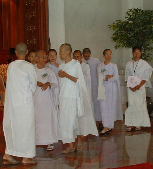 白いローブを着た9人のアジア人女性が立って話している。8人は髭を剃っているが、1人は剃っていない。
