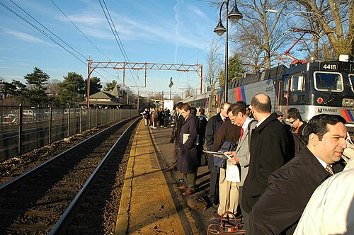 たいていの男性は、左側に空の線路があり、背後に列車と葉のない落葉樹がある駅で待っています。