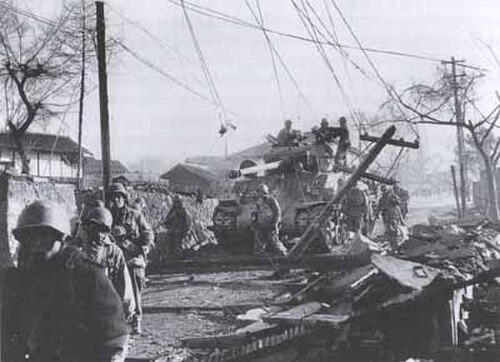 戦車を従えて、損傷した村を進む兵士たち