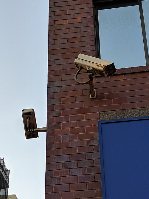 レンガ造りの建物の角に、異なる方向を向いた2台の監視カメラが設置されている。