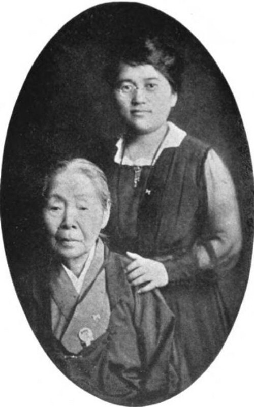 楕円形の肖像画のフレームに収められた 2 人の日本人女性。立っている女性は若い女性で、洋服を着て眼鏡をかけており、その手は和服を着た年配の女性の肩に置かれています。