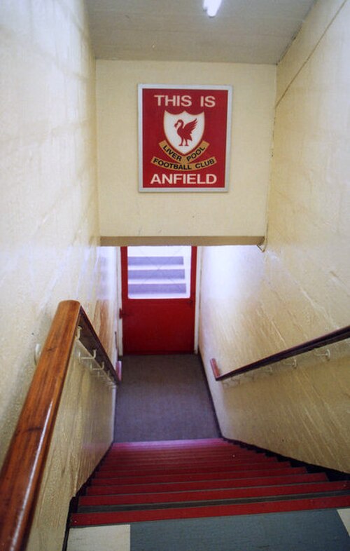 トンネルに下りる階段。トンネルの上には赤い背景に白い文字で「This Is Anfield」と書かれた看板があり、その上に紋章が描かれている。