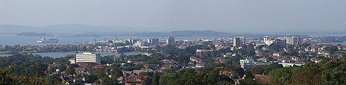 パークストーンから見たプール市街中心部のパノラマ写真。木々の間から高層ビル群と低層ビルの屋根が見え、その向こうの港には船が停泊している。