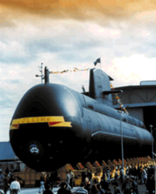 大きな建物から出てきた潜水艦。潜水艦には国旗が飾られ、正面には「COLLINS」の文字が描かれている。潜水艦の基部には数人の人々がいる。