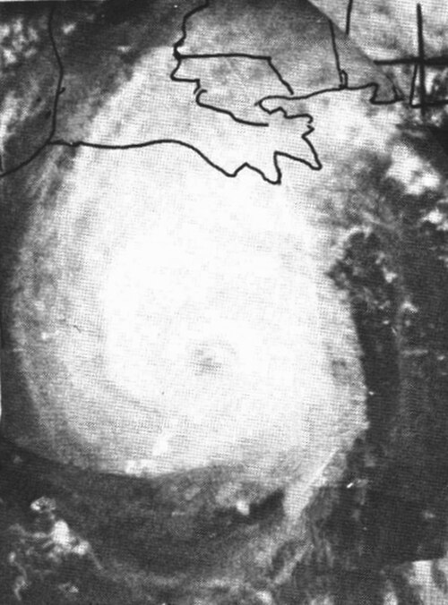 わずかに細長い熱帯低気圧の白黒画像。中心にかすかに目が見えます。雲は白く、陸地と水域は濃い灰色で表示されます。