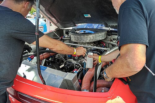 キャブレターが付いた V8 エンジン。エンジンの両側で 2 人の男性が作業しています。