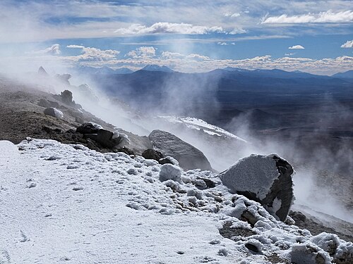 雪に覆われた山の斜面には蒸気雲が覆い、背景には山の風景が広がっています。