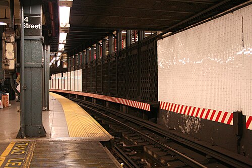 IRTレキシントン・アベニュー線14丁目-ユニオン・スクエア駅の南行き各駅停車ホームの様子。右側の壁と黒い柵の向こうには、かつて使われていた側線ホームがあり、その端がまだ見える。その真上には中二階がある。赤と白の縞模様は、列車と壁の間に隙間がないことを示している。手前には、近接センサーで自動的に作動する隙間埋め装置が見える。床には「離れてください」と書かれている。