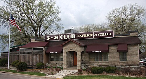 ワインレッド色の日よけと「5-8 Club Tavern & Grill」の看板がある1階建ての石造りの建物