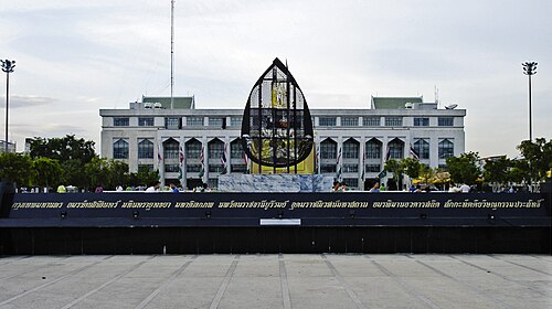 タイ文字で長い名前が書かれた花崗岩の看板と、その背景にある建物